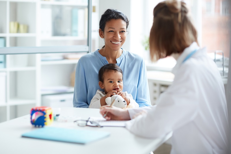 Mother with baby speaking to doctor in white coat.