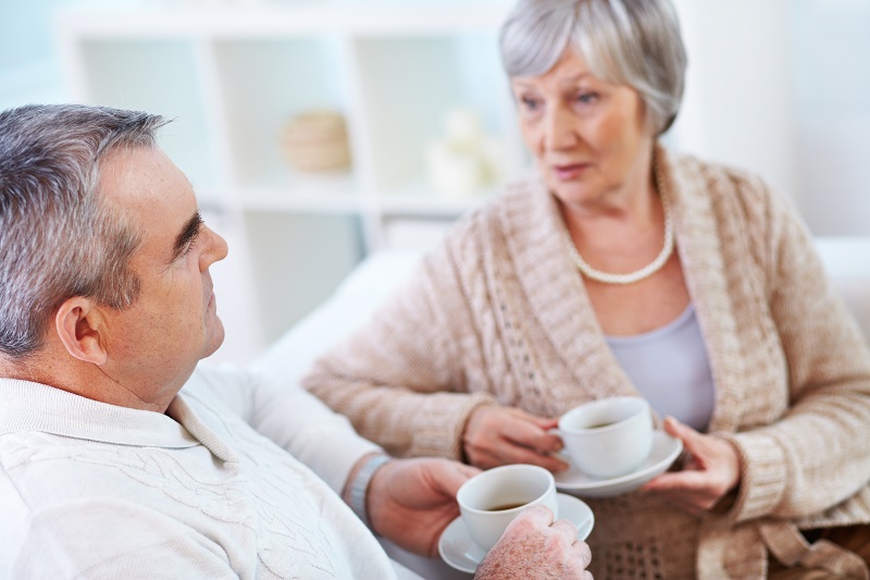 Older couple with grey hair talking while drinking tea.